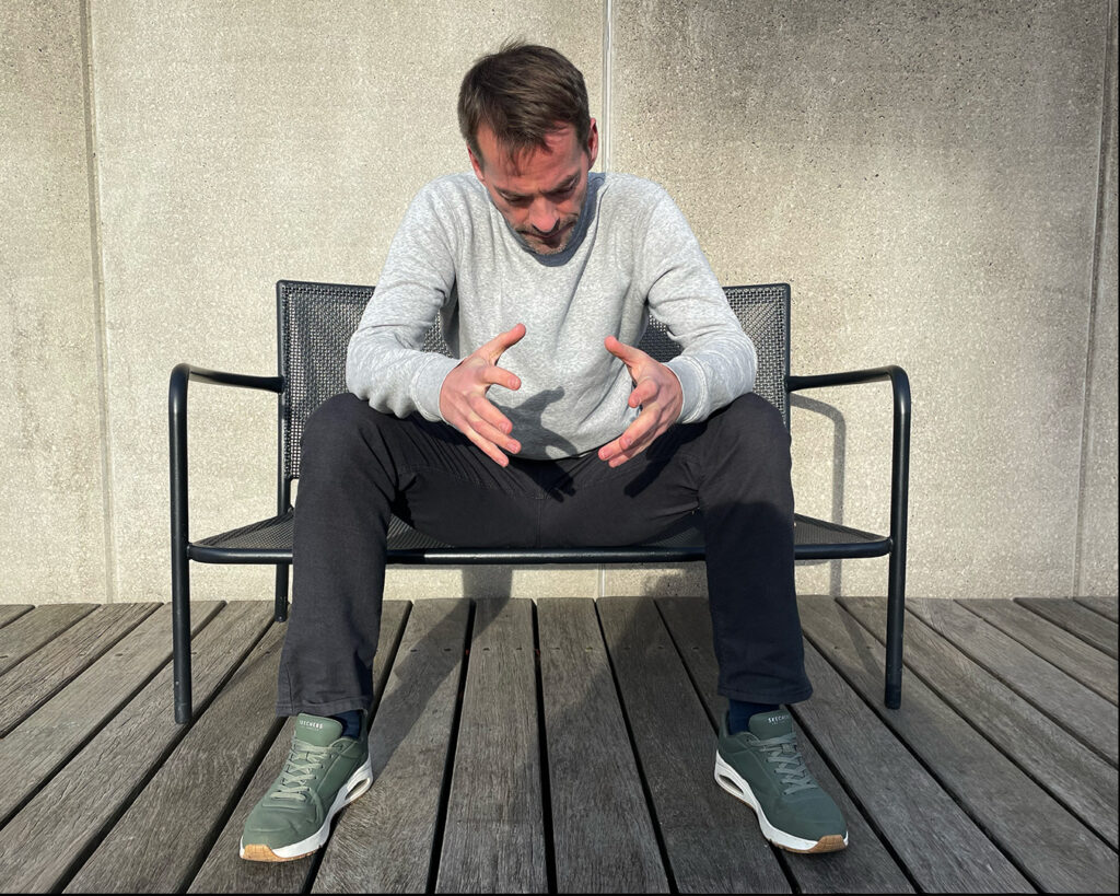 Psykoterapeut siddende på en bænk ved havnen i København, dybt optaget af et eksistentielt fænomen.